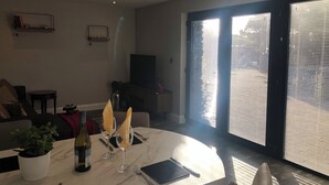 Una sala de estar moderna con comedor, televisor y un amplio ventanal corredera al exterior.