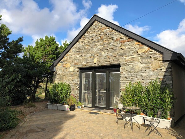 Un bâtiment en pierre avec un toit en pente, une grande porte vitrée et des plantes en pot au premier plan.