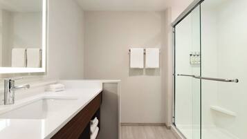 Un baño moderno con cabina de ducha de vidrio, un lavamanos blanco y un espejo.