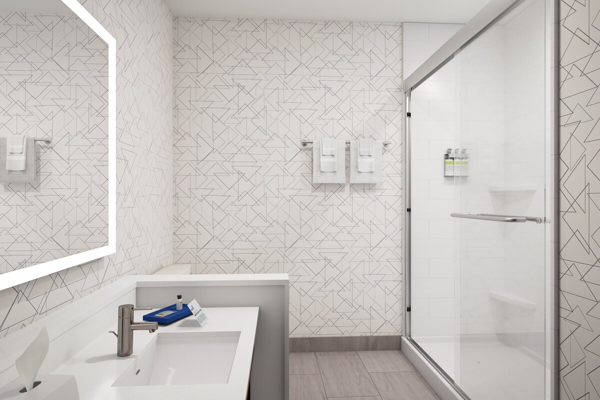 Ein modernes Badezimmer mit einem geometrischen Fliesenrückwand, einem weißen Waschbecken mit einer blauen Seifenschale und einer Glasdusche.