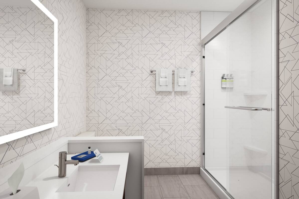 Un baño moderno con un salpicadero de azulejos geométricos, un lavamanos blanco con un jabonera azul y un box de ducha de vidrio.