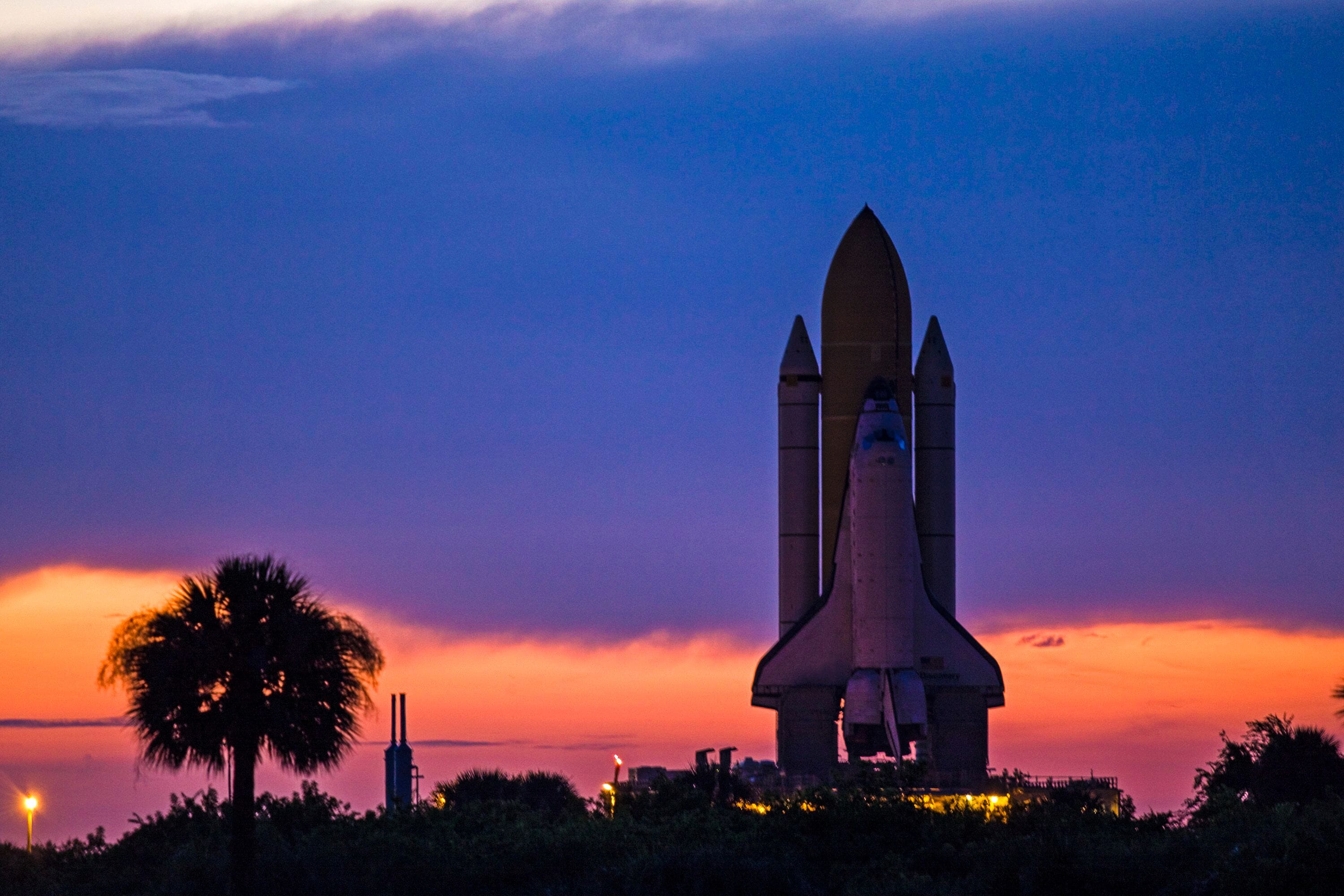 Un transbordador espacial al atardecer, con un cielo despejado y palmeras al frente.