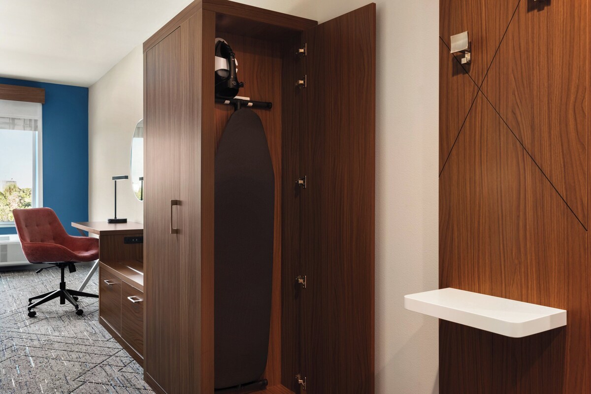Ein Zimmer mit einem Holzschrank, einem Schreibtisch mit Stuhl und einem weißen Regal.