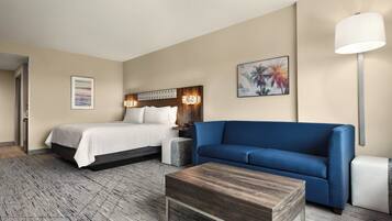 Una habitación de hotel con una cama, un sofá azul, una mesita de centro de madera y una mesita de noche con lámpara.