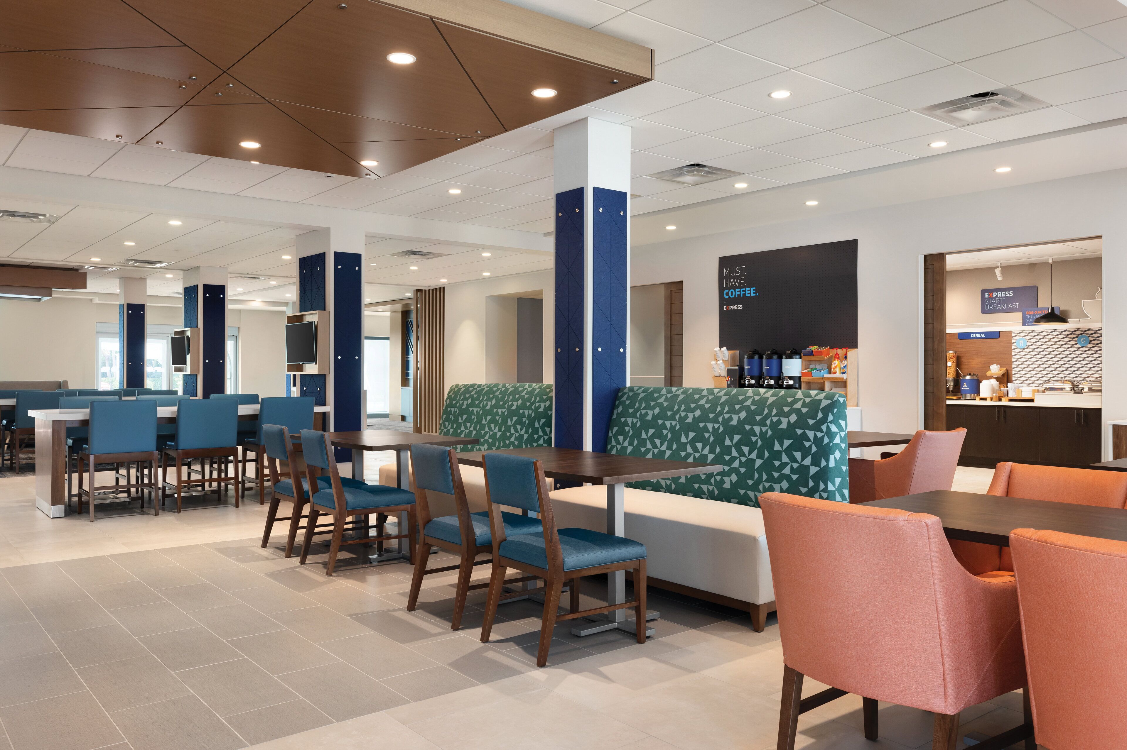 A modern hotel lobby with seating areas, a coffee bar, and a visible kitchen area.