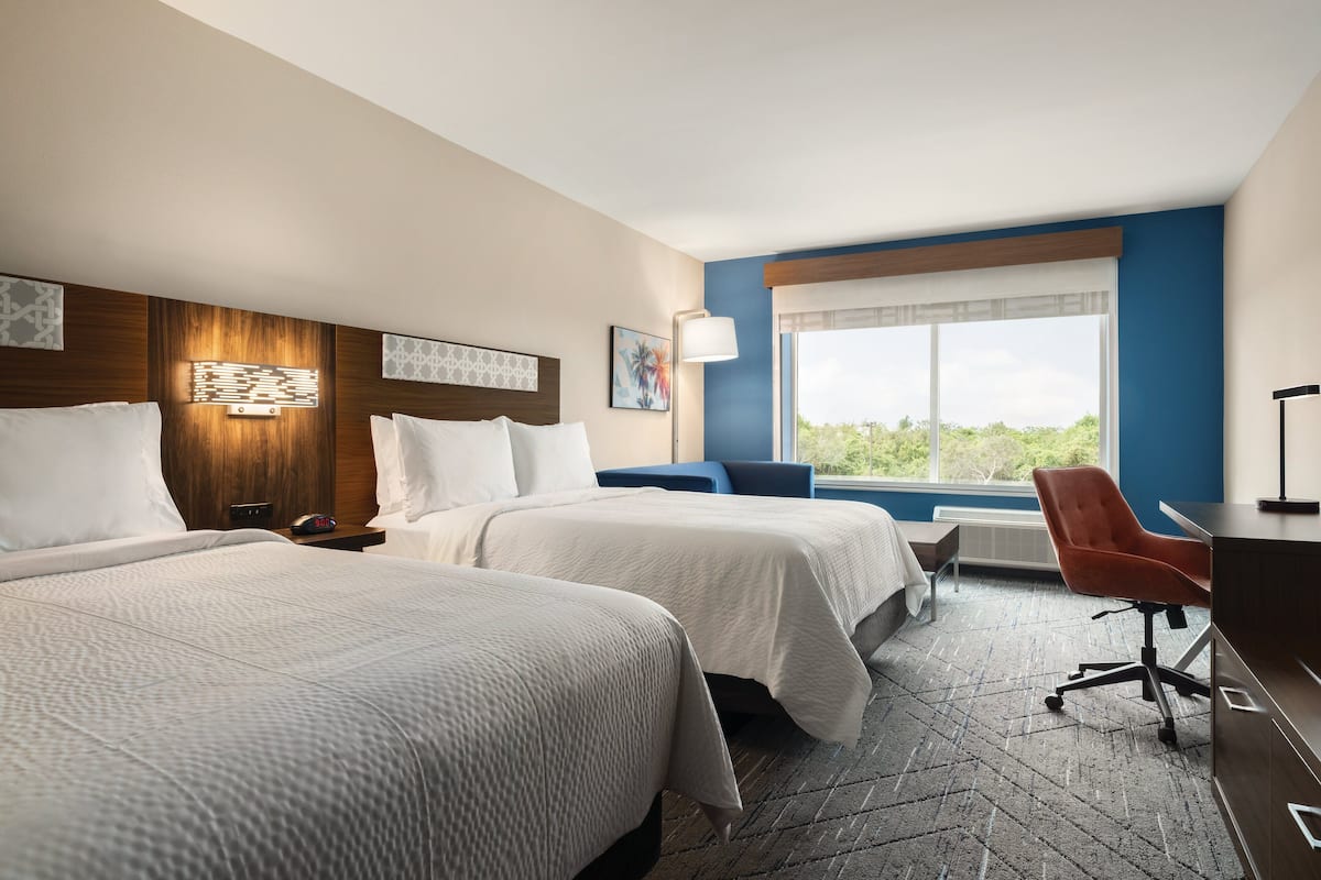Une chambre d’hôtel avec deux lits, un bureau, une chaise et une grande fenêtre donnant sur un paysage agréable.