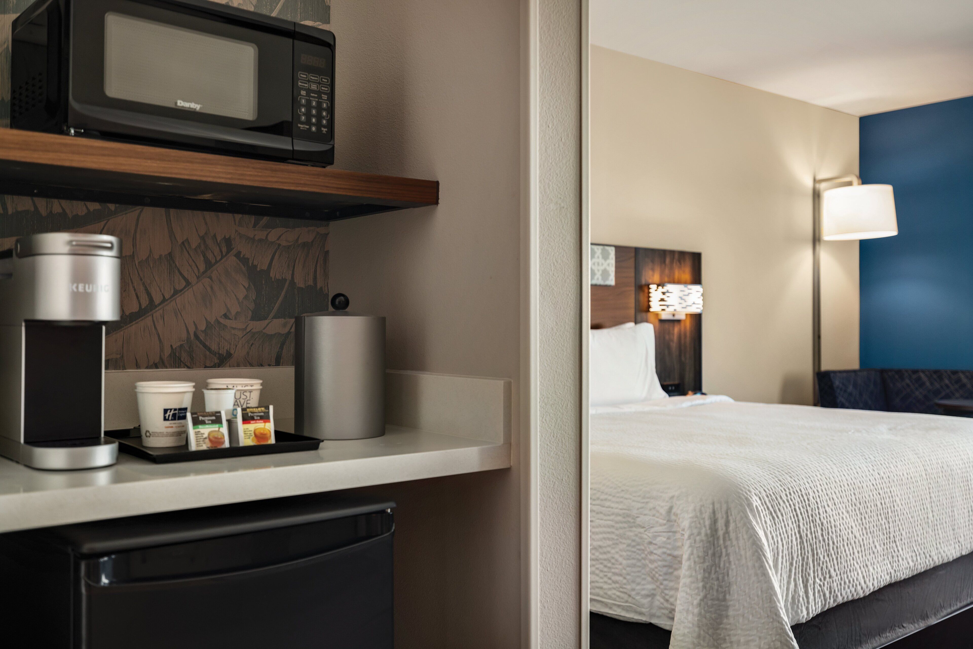 A hotel room with a bed, a microwave, a coffee maker, and a small refrigerator.