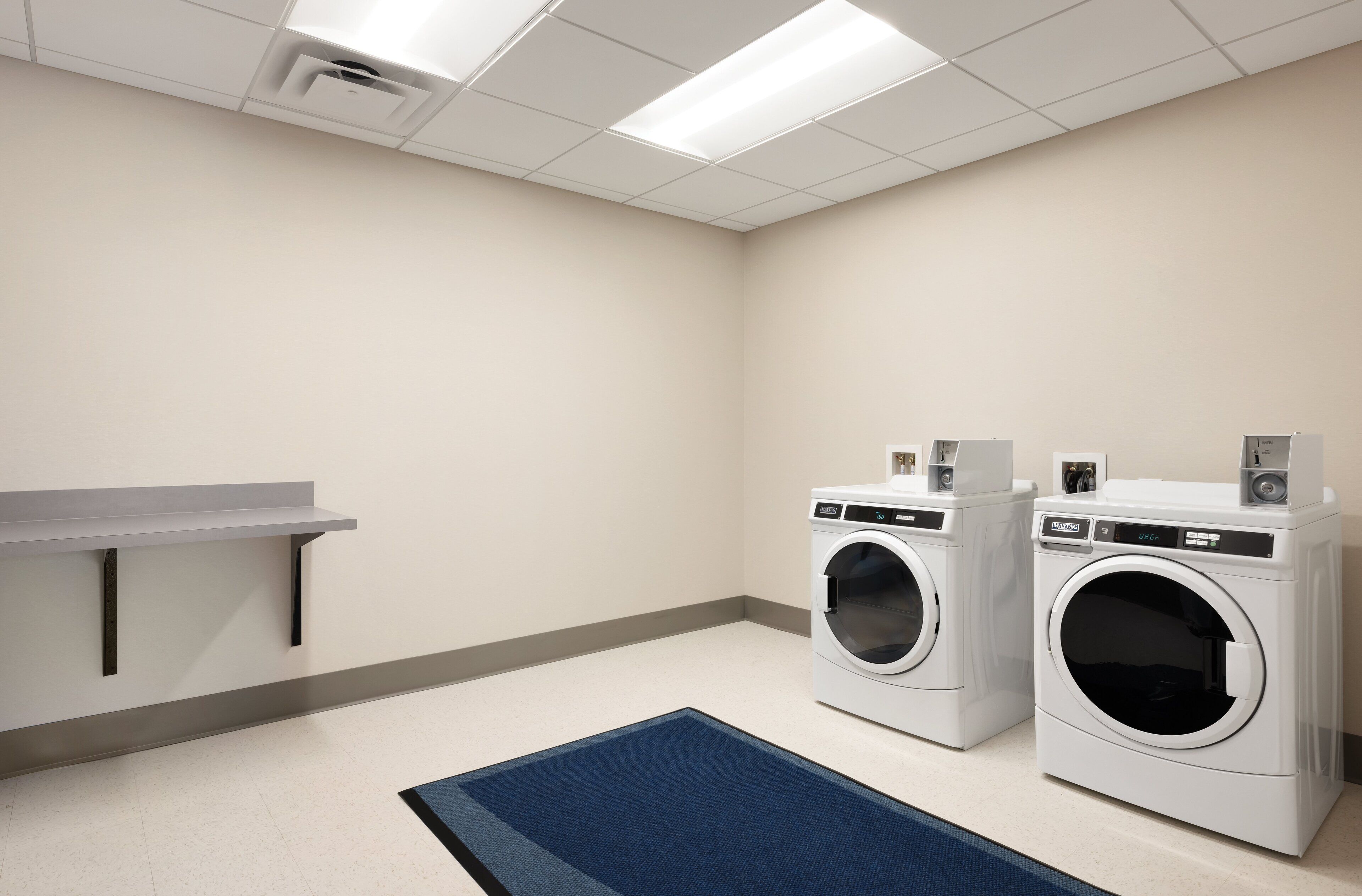 A laundry room with two front-loading washing machines, a small table, and a blue rug.
