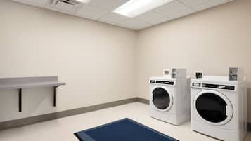 A laundry room with two front-loading washing machines, a small table, and a blue rug.