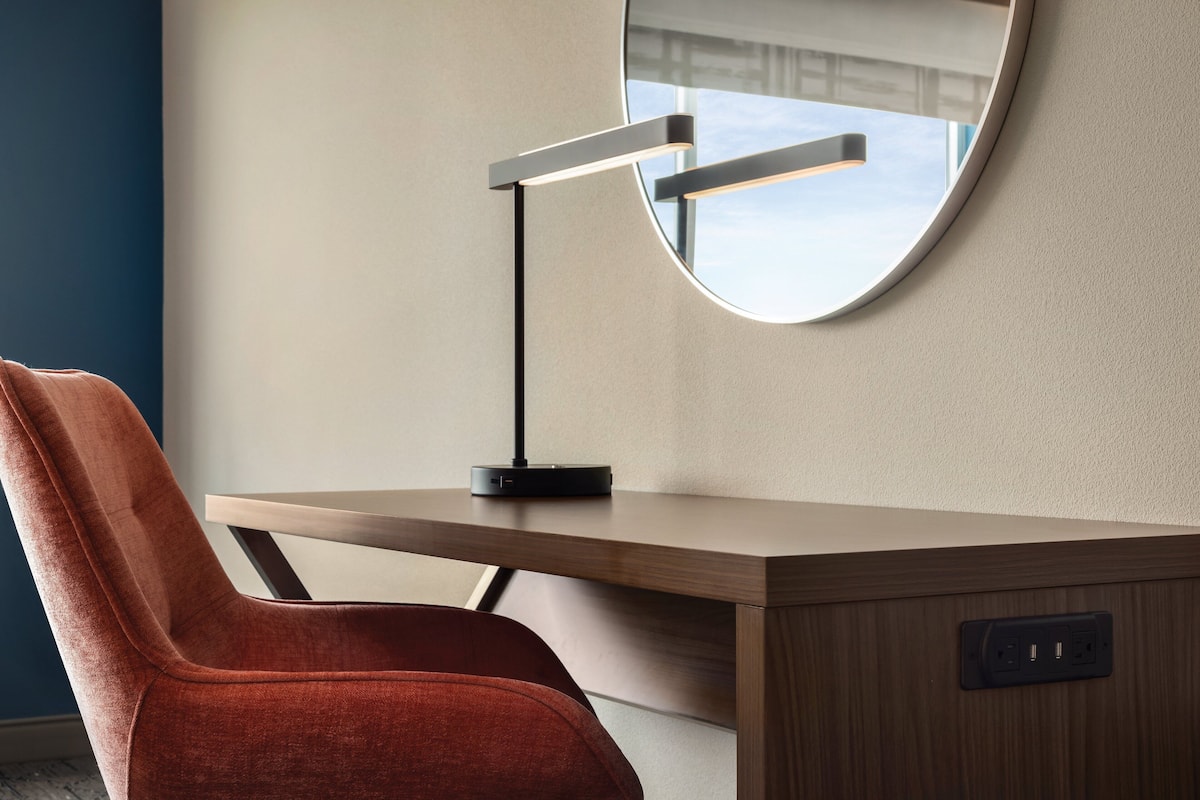 Un bureau moderne avec un miroir rond, une chaise rouge et une lampe noire.