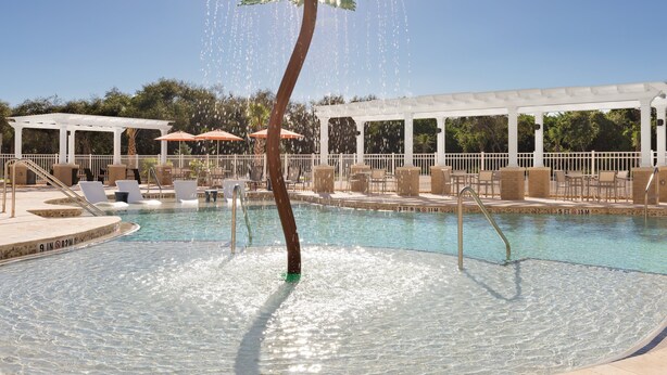A pool with a water feature resembling a palm tree, surrounded by lounge chairs and umbrellas. - Holiday Inn Express Cape Canaveral by IHG (Cape Canaveral)