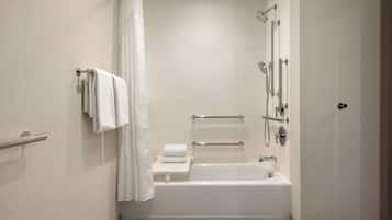 A modern bathroom with a bathtub, shower, and handrails.