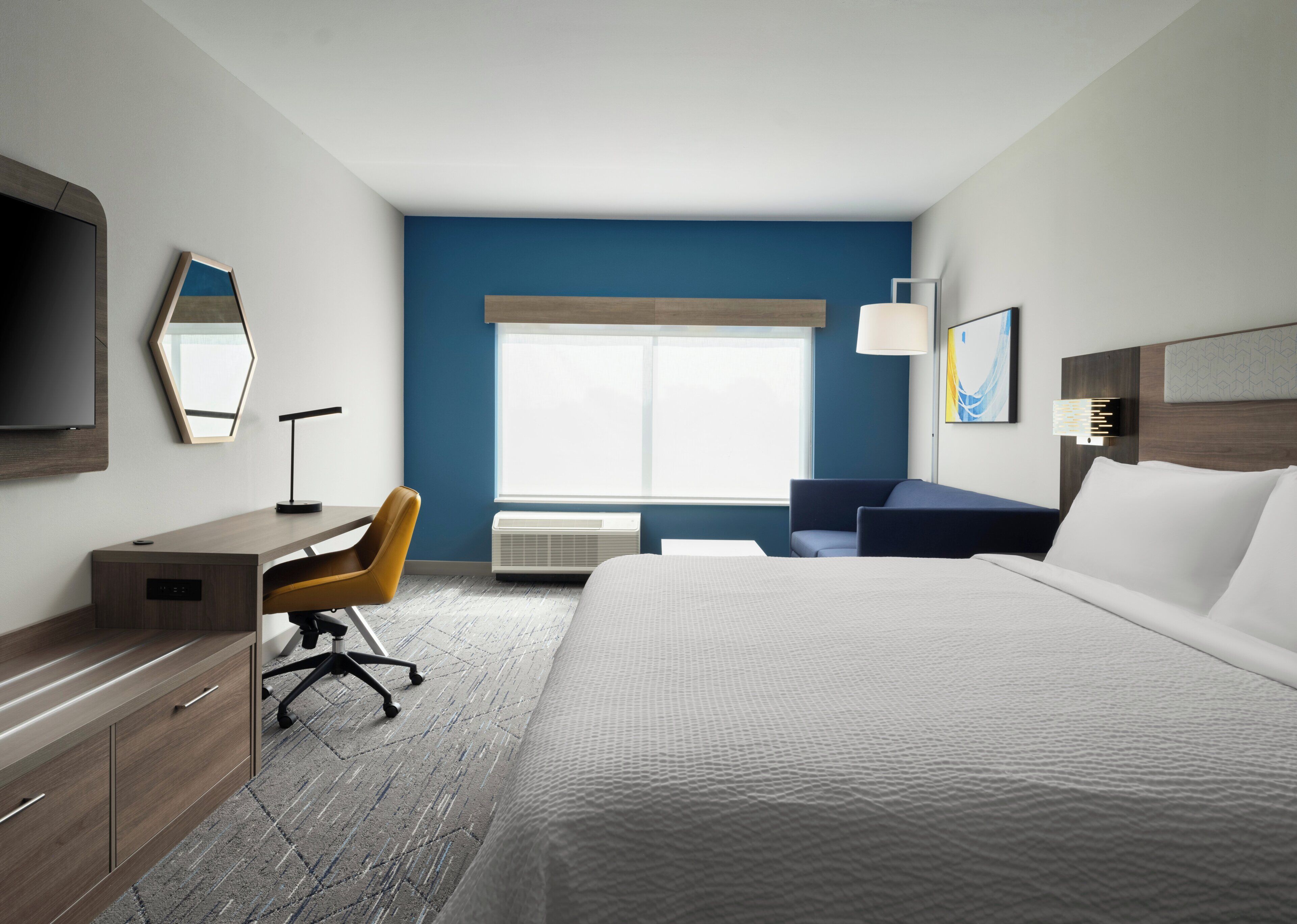 Habitación de hotel con cama, escritorio, silla y un ventanal amplio.