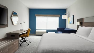 A hotel room with a bed, desk, chair, and a large window.