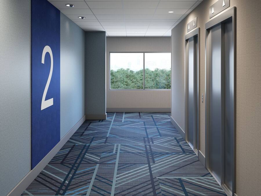 Un couloir avec un mur bleu, une plaque portant le chiffre « 2 », une moquette à motifs et un ascenseur.