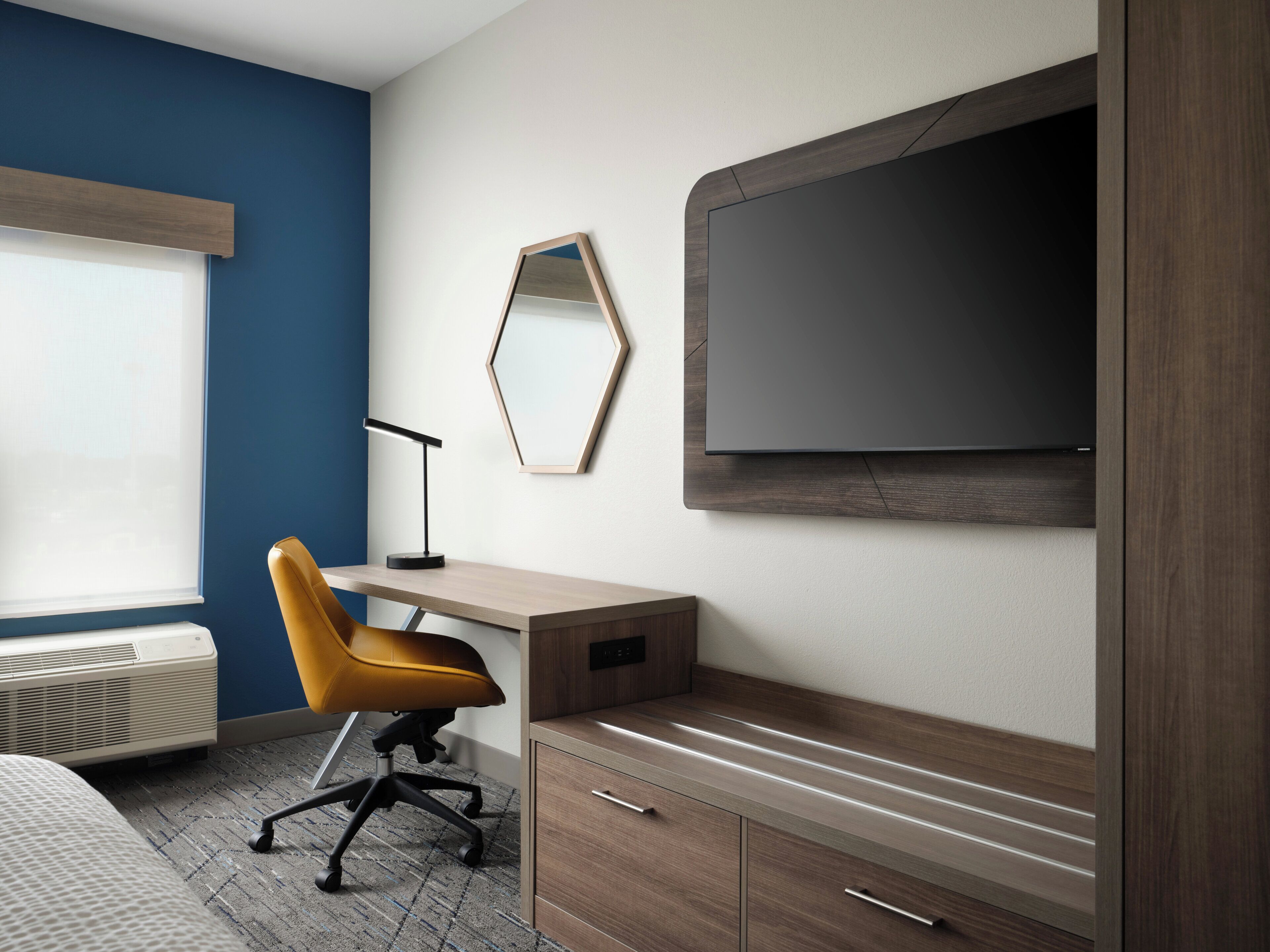 A hotel room with a bed, a desk, a chair, a TV, and a mirror.