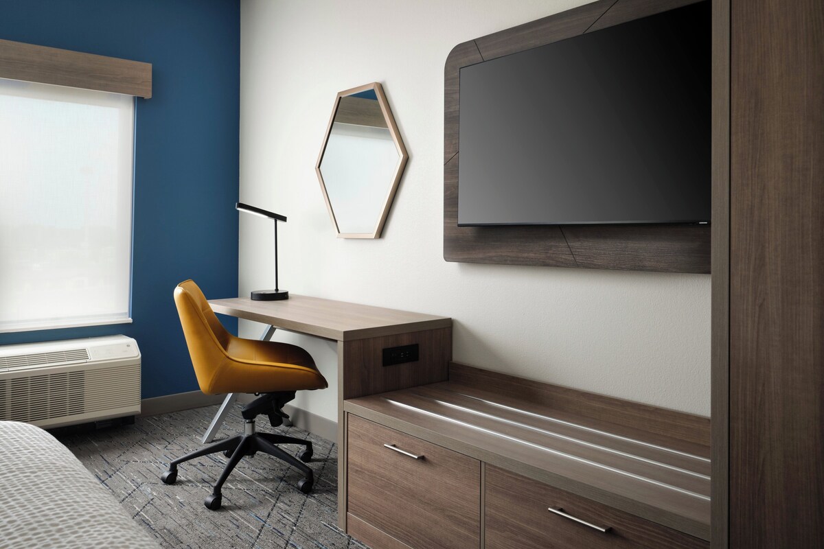 Een moderne hotelkamer met een bed, een bureau, een stoel, een televisie en een spiegel.