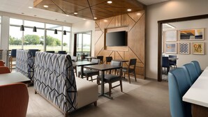 A modern dining area with a high ceiling, geometric wall design, and a flat-screen TV mounted on the wall.