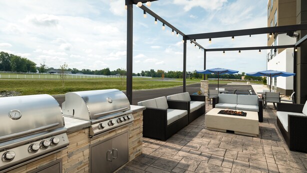 An outdoor patio with a grill, seating, and a view of a field.