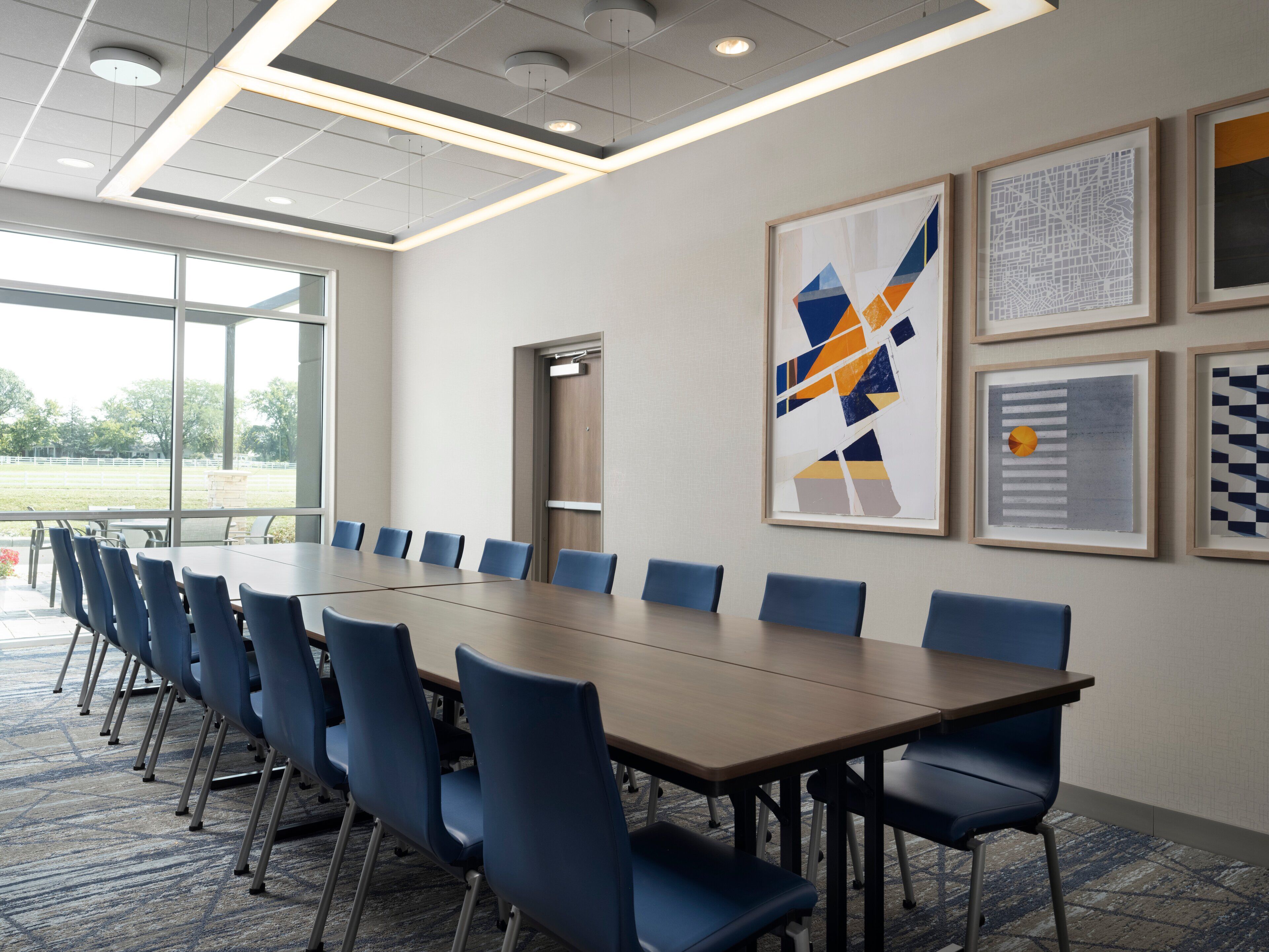 A conference room with a long table and blue chairs, large windows, and abstract art on the walls.