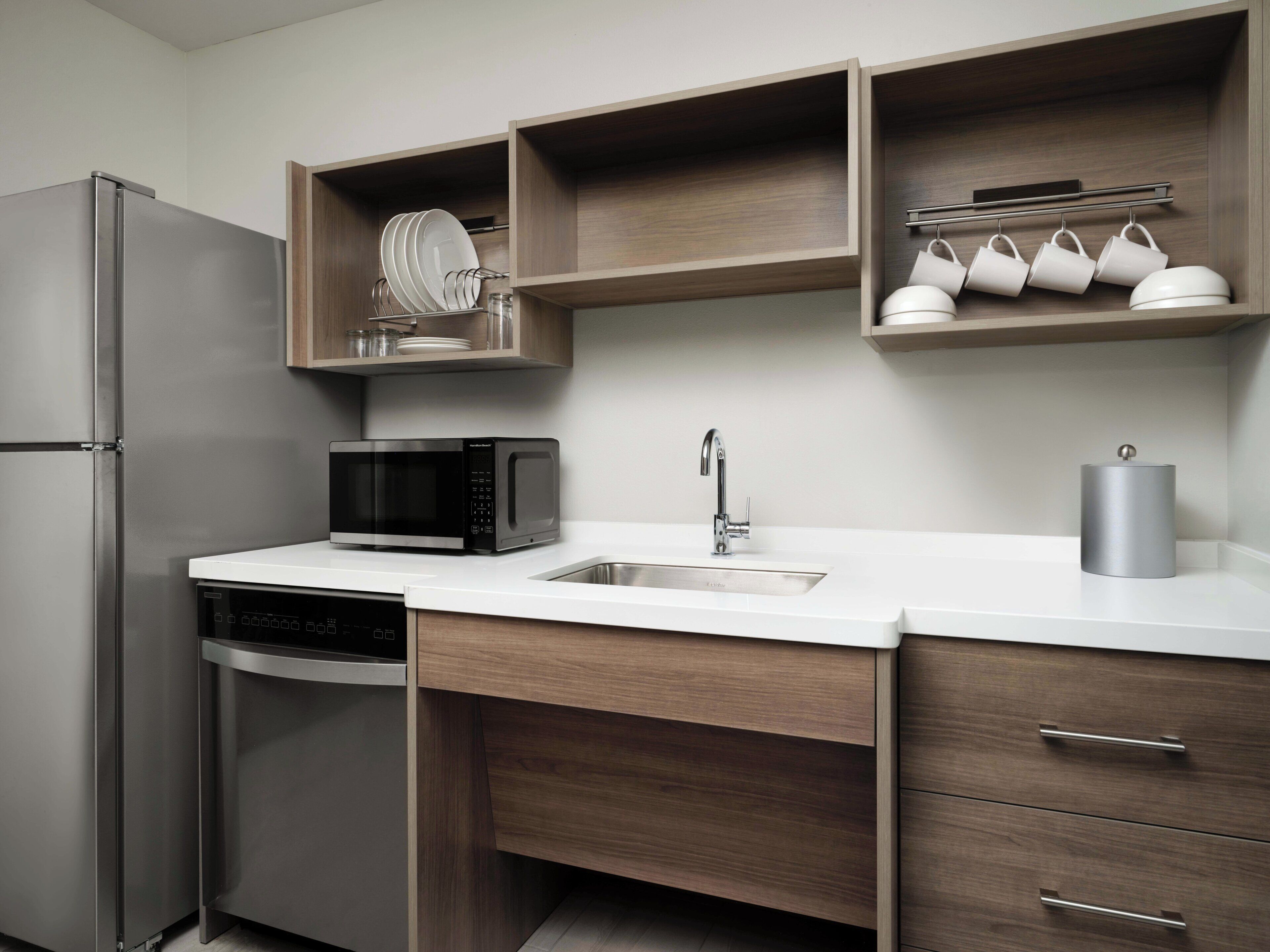 A modern kitchen with a stainless steel refrigerator, a black microwave, a sink, and wooden cabinetry.