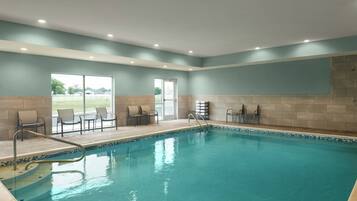 Une piscine avec une terrasse carrelée, des chaises et une porte vitrée donnant sur l’extérieur.