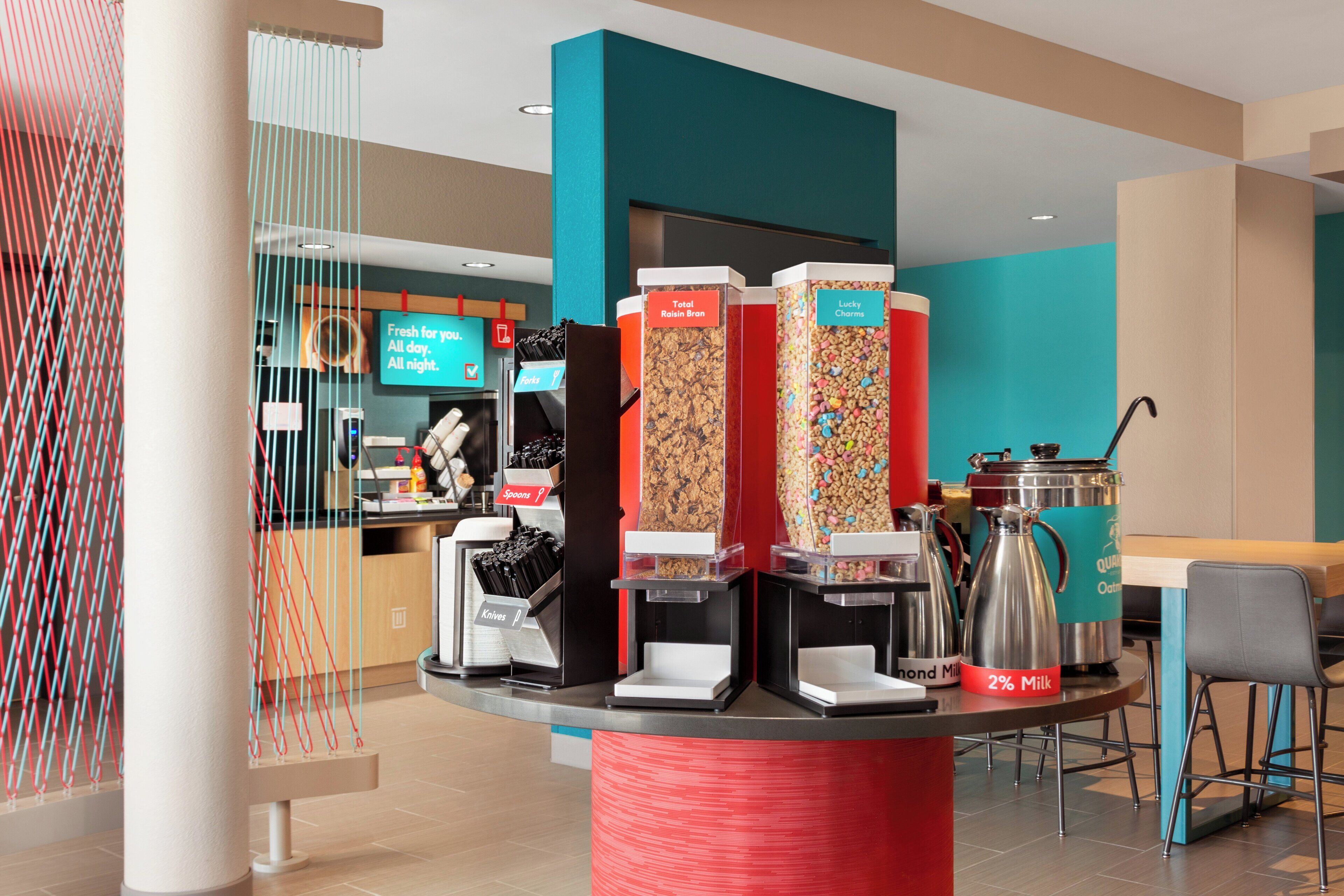 Una barra de desayuno con distintos dispensadores de alimentos, una máquina de café y un hervidor.