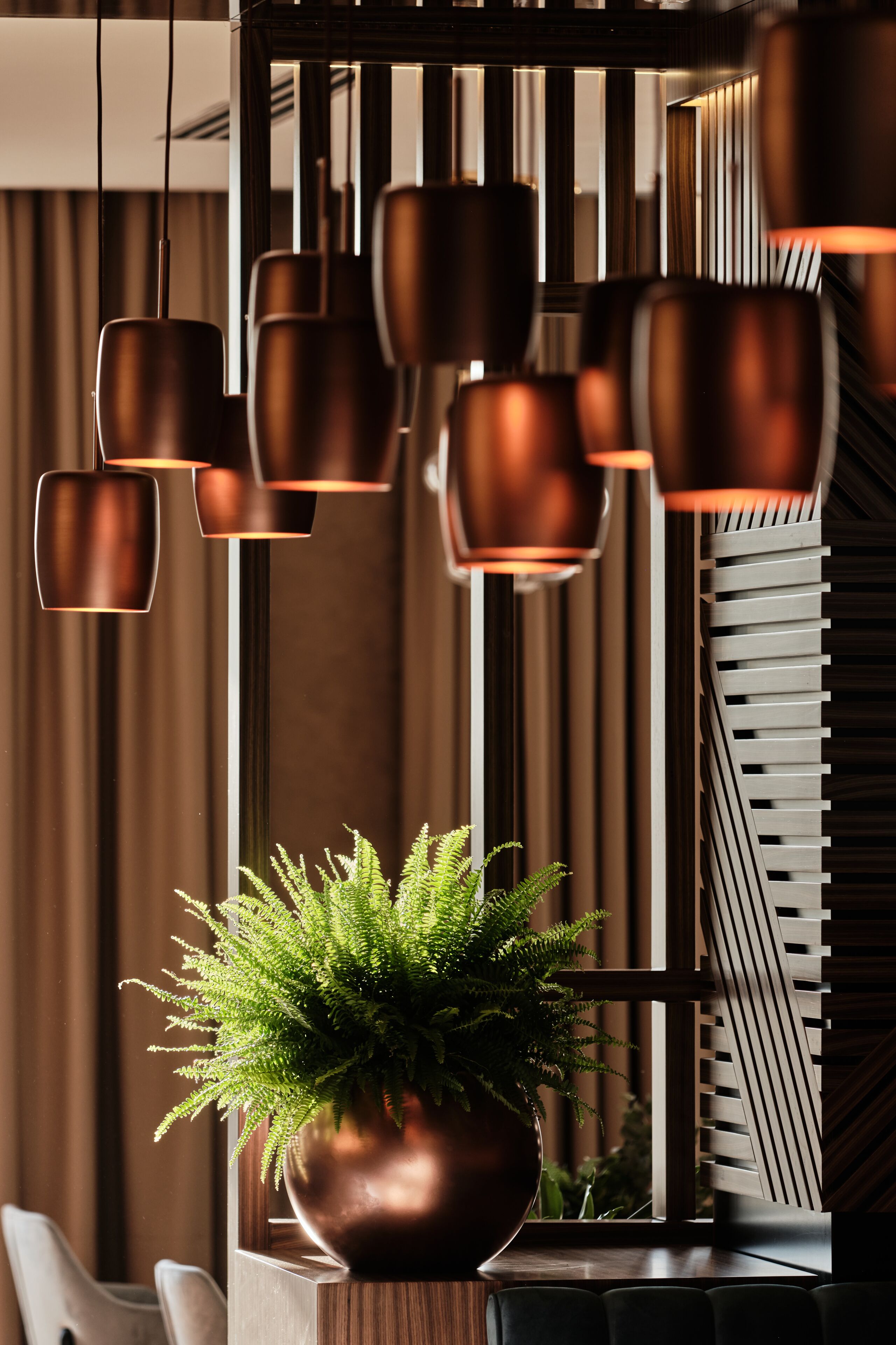 A modern interior with a large potted plant, multiple hanging copper pendant lights, and a contemporary chair arrangement.