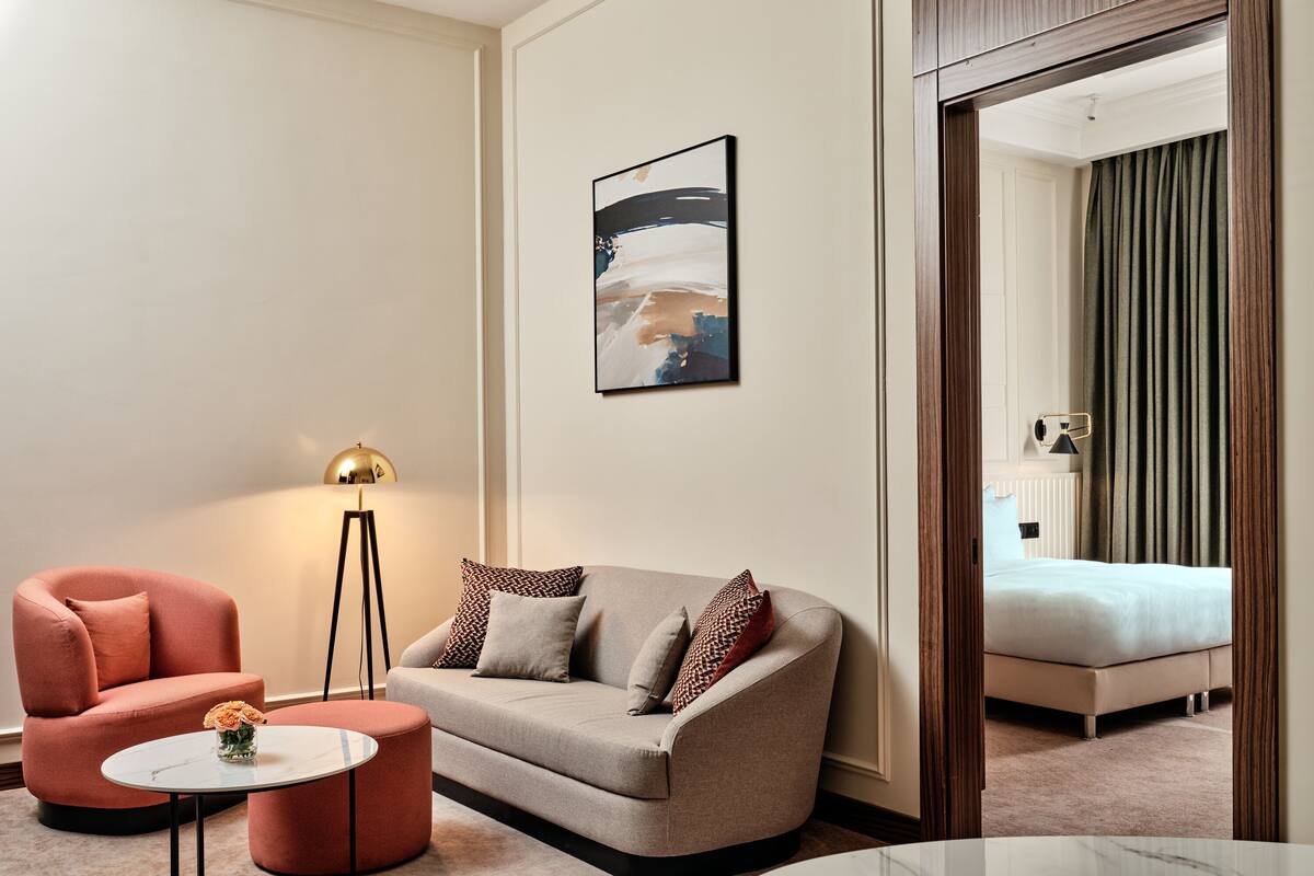 A modern hotel room with a sofa, armchair, and a small table with flowers.