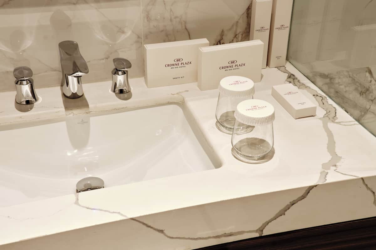 A bathroom with a white marble sink, chrome faucets, and vanity kits labeled 'Crowne Plaza.'