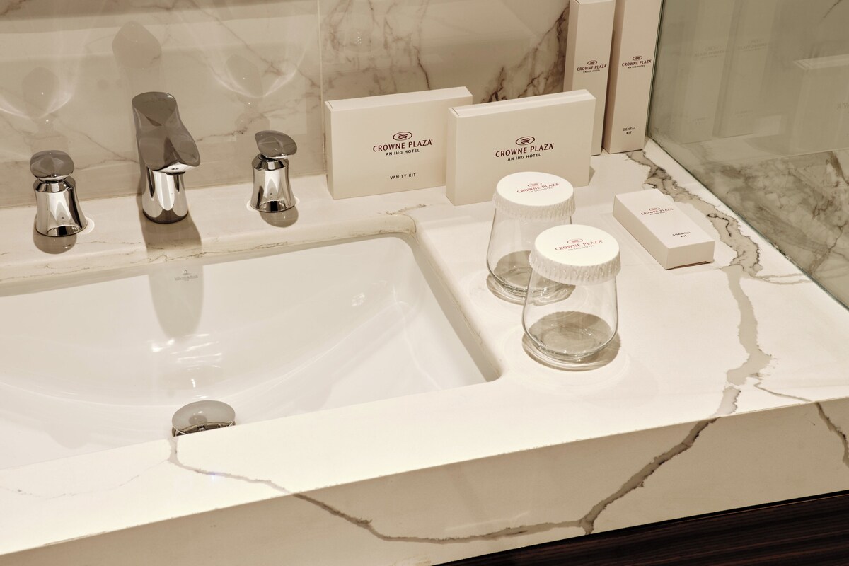 A bathroom with a white marble sink, chrome faucets, and vanity kits labeled 'Crowne Plaza.'
