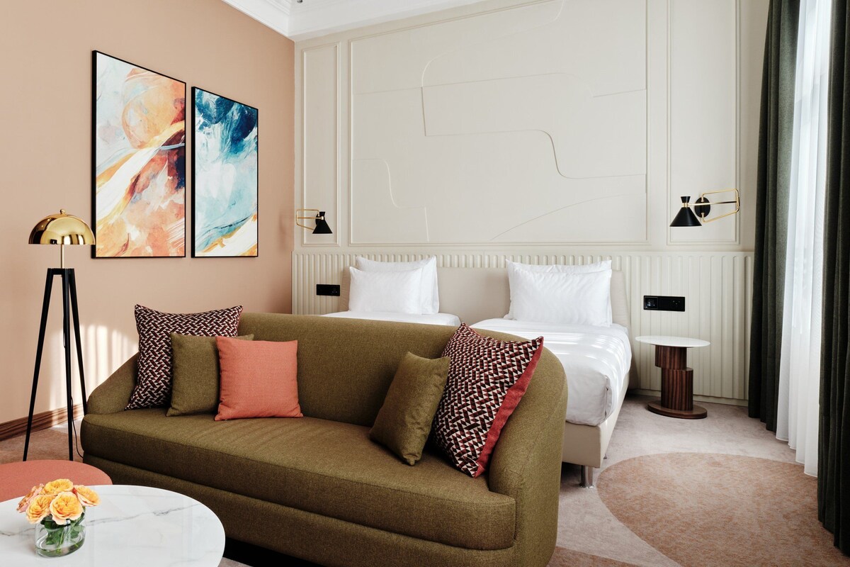A hotel room with a sofa, a bed, a small table, and a vase of flowers.