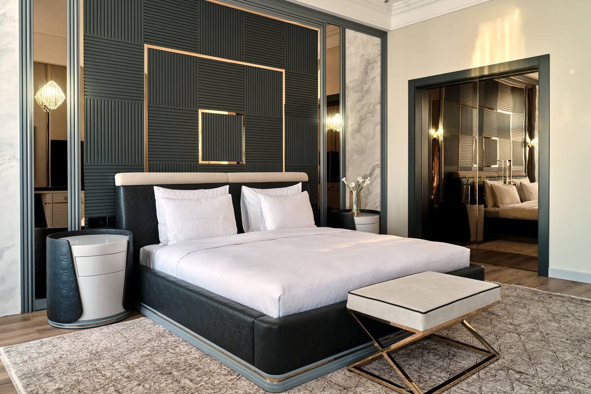 A modern bedroom with a large bed, bedside tables, a nightstand, and a seating area with a bench.