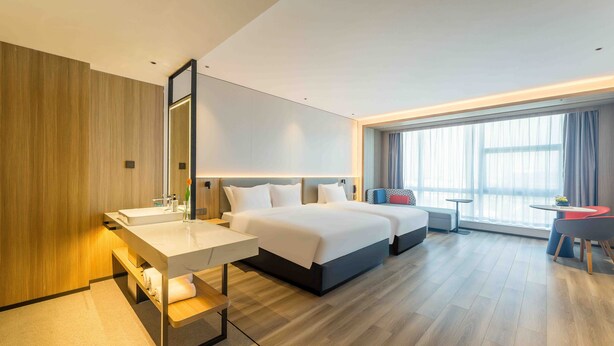 Una habitación de hotel moderna con una cama grande, una mesita de noche, un escritorio con espejo y una ventana con cortinas.