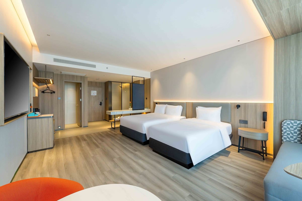A modern hotel room with two beds, a desk, a TV, and a bathroom.