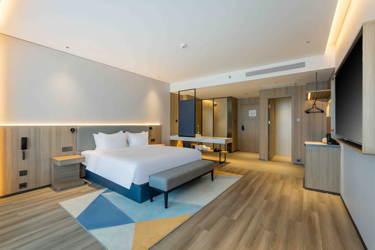 A modern hotel room with a large bed, bedside tables, a flat-screen TV, a mirror, and a walk-in closet.