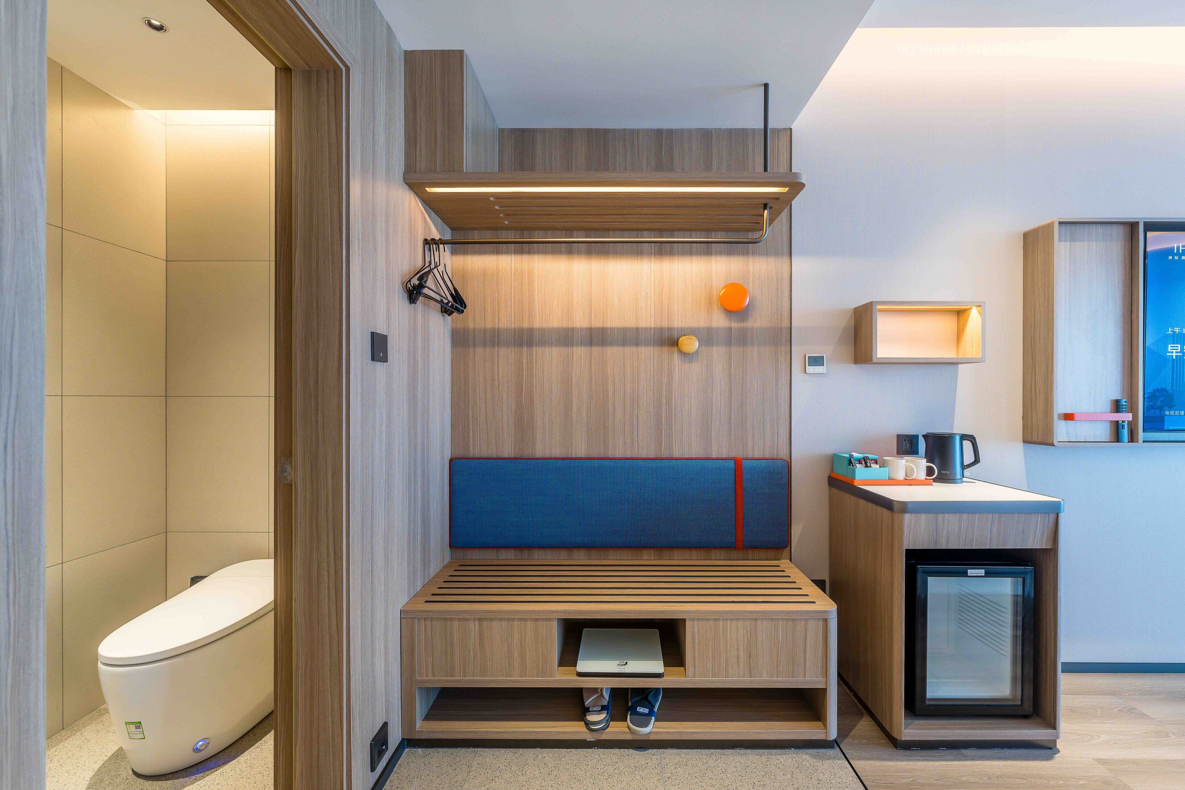 A modern bathroom with a built-in bench, a toilet, a sink, and a small refrigerator.