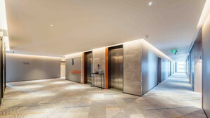 Un pasillo moderno de hotel con alfombra estampada, ascensores y una larga galería.