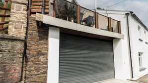A modern building with a stone facade, a metal staircase, and a closed roller shutter garage. - Greenheart Cottage (Port Talbot)