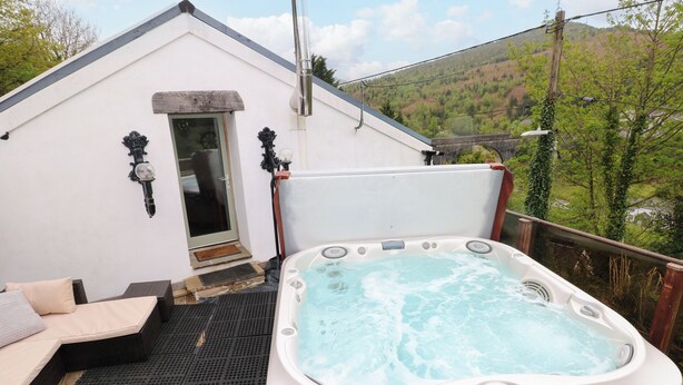 A hot tub on an outdoor deck with a view of a hillside. - Greenheart Cottage (Port Talbot)