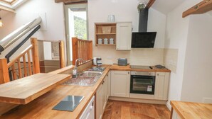 A modern kitchen with wooden countertops, a dishwasher, an oven, and a built-in TV. - Greenheart Cottage (Port Talbot)