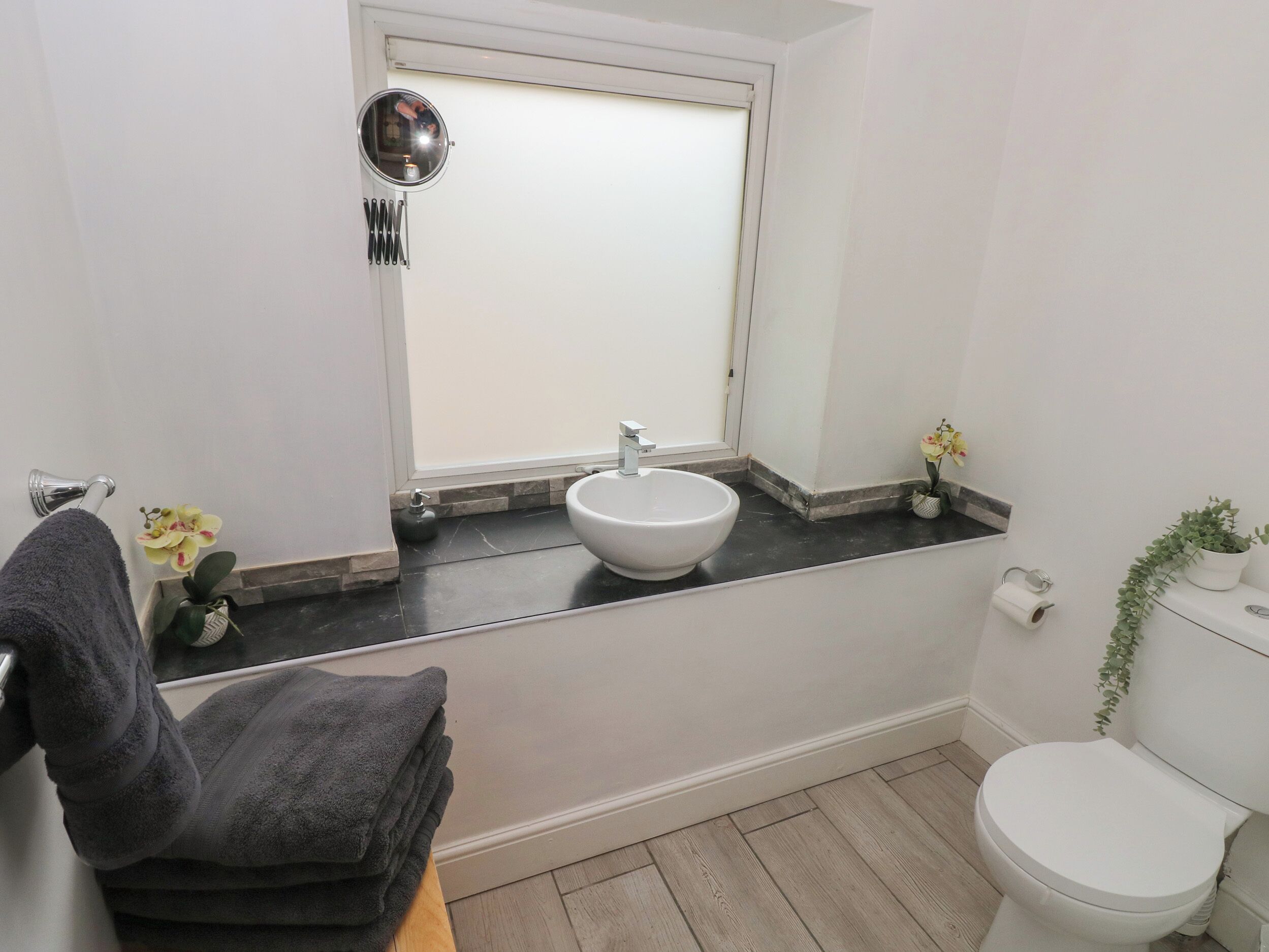 A bathroom with a white sink, a toilet, a mirror, and a window.