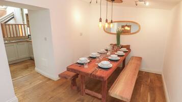 Un comedor con una mesa de madera dispuesta para seis personas, un banco y un espejo en la pared.