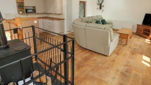 A spacious living area with a large beige sectional sofa, a wooden dining table, and a kitchen with wooden cabinets and a black stove. - Greenheart Cottage (Port Talbot)