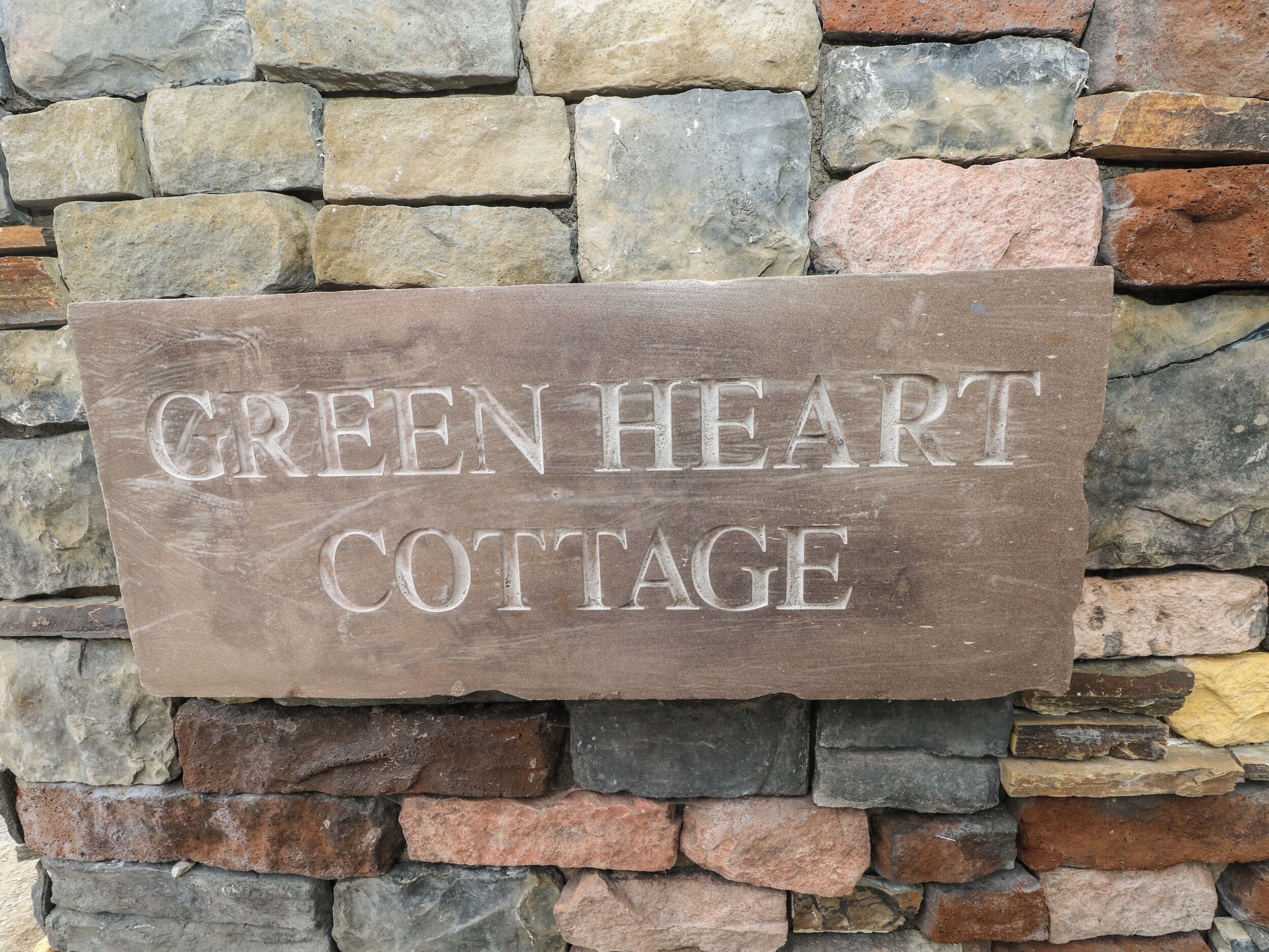 A stone sign with the text "GREEN HEART COTTAGE" mounted on a stone wall.