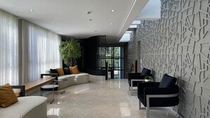 A modern living room with a curved sofa, black chairs, and a geometric wall design. - Studio ID Lisboa (São Paulo)