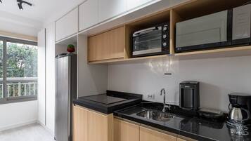 Cocina moderna con horno empotrado, microondas y cafetera, que presenta armarios de madera y encimera negra.