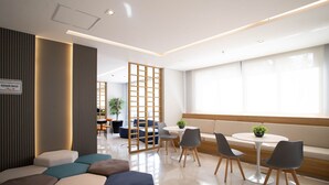 A modern lounge area with seating arrangements, a small table with chairs, and a partition with a sign indicating an elevator service area. - Studio ID Lisboa (São Paulo)