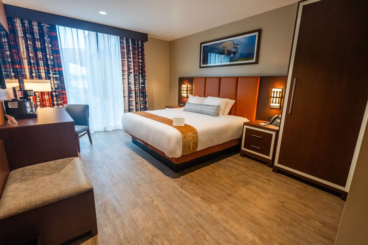 A hotel room with a large bed, a desk, a chair, a nightstand, and a wardrobe.