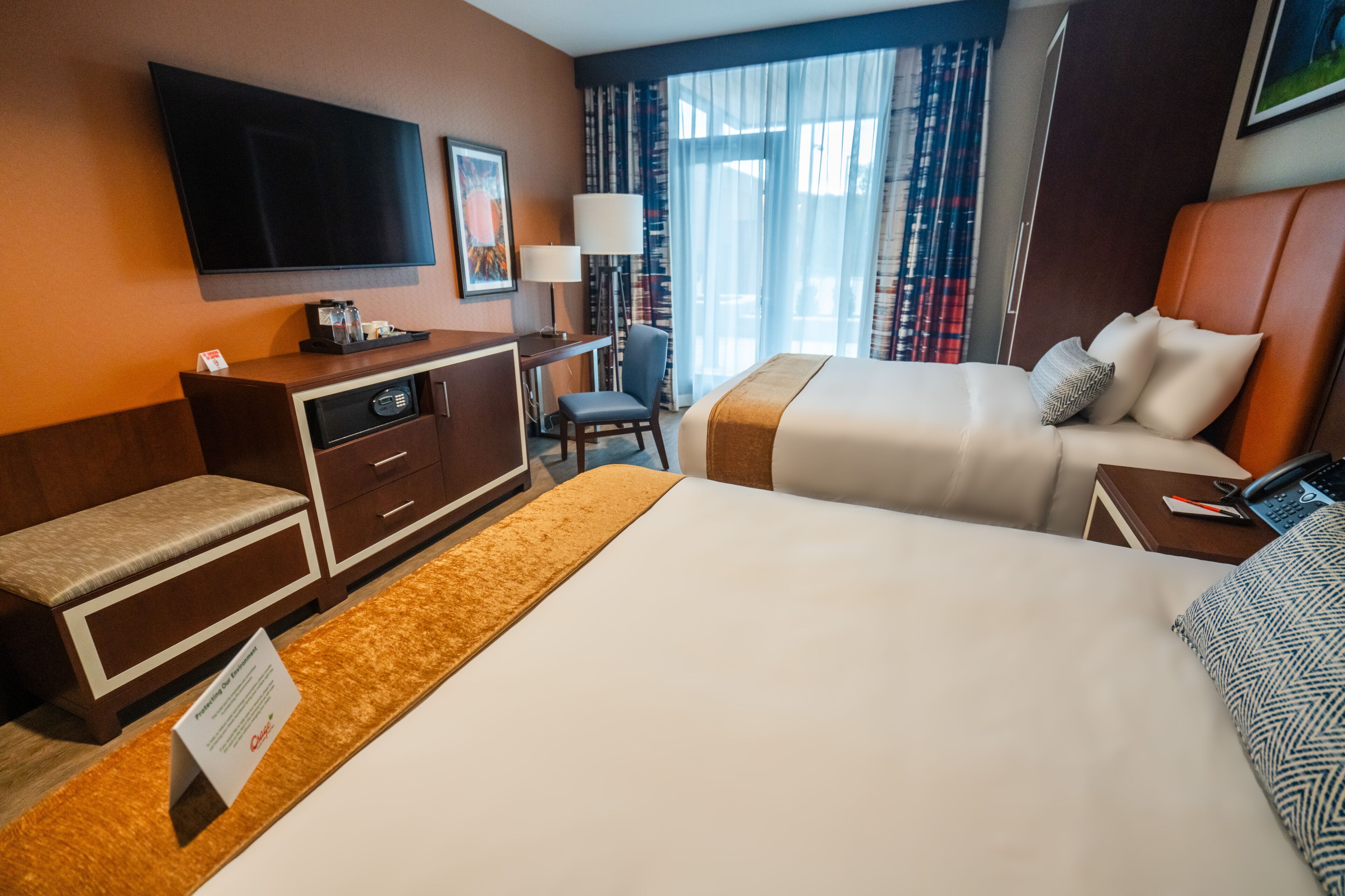 A hotel room with a large bed, a desk with a chair, a television mounted on the wall, and a window with curtains.